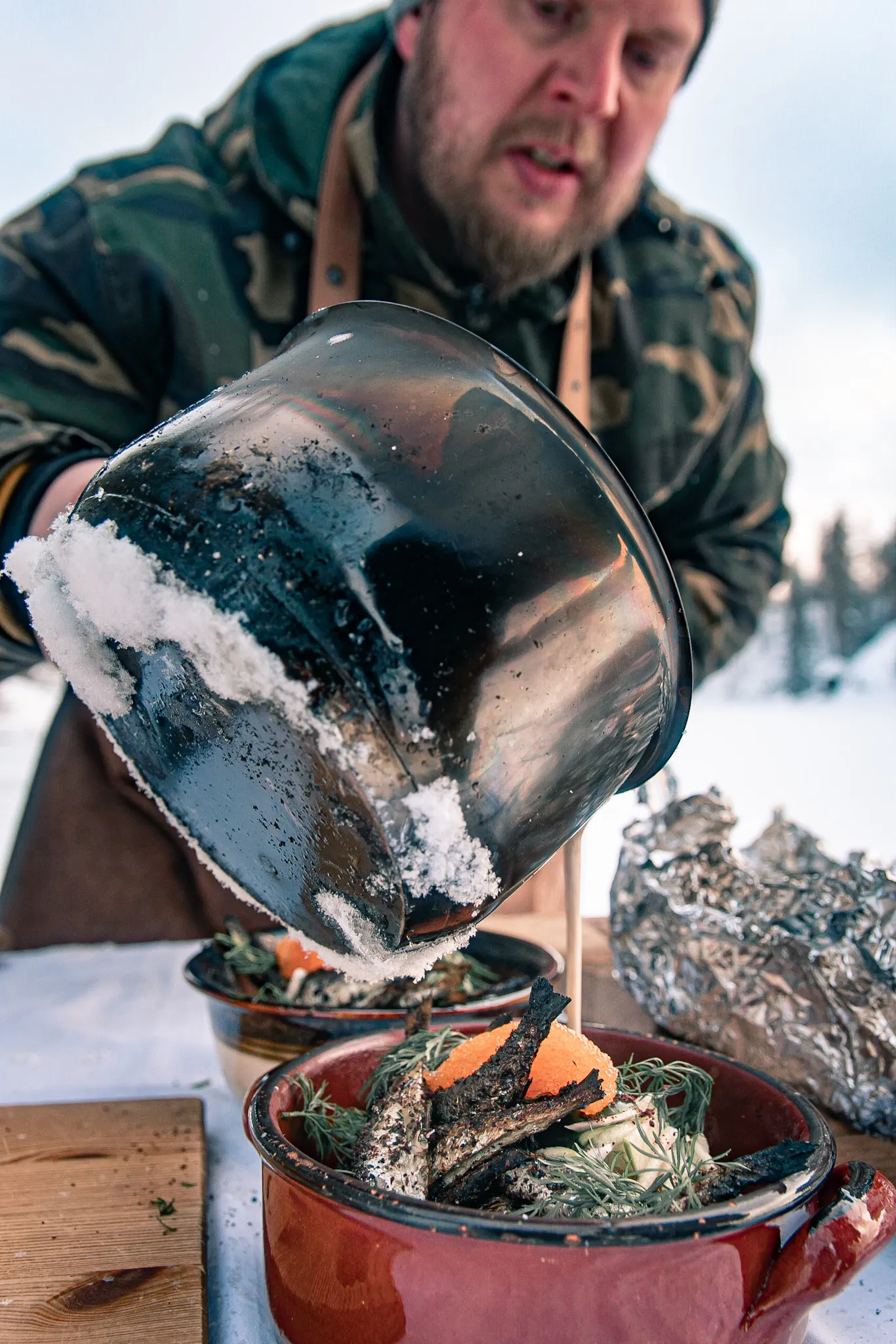Mies kaataa ruoan pannusta punaisiin ruokalautasiin ulkona talvimaisemassa.